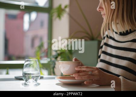 Eine Frau, die in einem Café sitzt und eine Tasse Kaffee trinkt Stockfoto