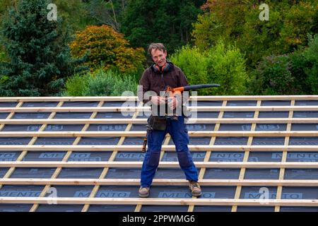 Arbeiter steht auf dem Dach, nachdem er sich über der Isolierung des zu renovierenden Hauses versammelt hat Stockfoto