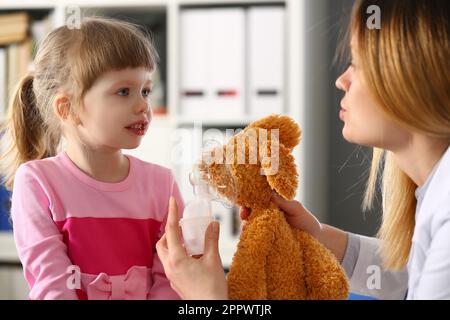 Der Kinderarzt zeigt dem kleinen Mädchen auf dem Spielzeug, wie man die Sauerstoffmaske benutzt Stockfoto