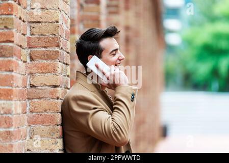 Junger Mann in Winterkleidung auf der Straße. Junger Mann mit moderner Frisur mit braunem Mantel. Stockfoto