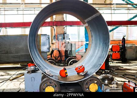 Das Verfahren zur Herstellung eines zylindrischen Behälterkörpers, eines Wärmetauschers auf Rollen, durch Walzen, Schweißen und orangefarbene Helme in der Industrie p Stockfoto