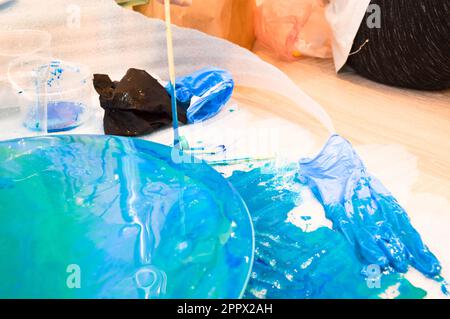 Der Prozess, ein hausgemachtes, modernes, abstraktes Muster zu kreieren, das mit einem Pinsel aus mehrfarbigem Acrylharz auf einem runden Holzbrett bemalt wurde. Stockfoto