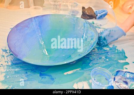 Ein Mann mit blauem Handschuh malt wunderschön ein mehrfarbiges Acrylharz auf einem runden, selbstgemachten Brett. Stockfoto