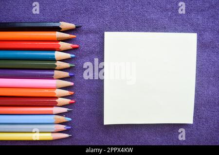 Mehrfarbige, leuchtende, farbenfrohe Bleistifte zum Zeichnen auf der linken Seite und ein Blatt Papier auf der rechten Seite für Ihren Text auf violettem Hintergrund. Stockfoto