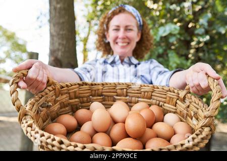 Porträt einer lächelnden reifen Landwirtin mit Weidenkorb und braunen Eiern in der Geflügelzucht Stockfoto