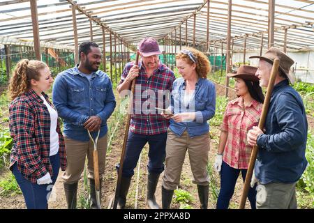 Multikulturelle männliche und weibliche Landwirte diskutieren über einen Tablet-PC, während sie im Betrieb mit Werkzeugen stehen Stockfoto