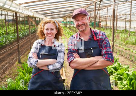 Porträt lächelnder reifer Bauern und Bauern, die im Bauernhof mit überkreuzten Armen stehen Stockfoto