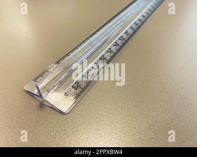 Ein durchsichtiges, langes Zentimeterlineal liegt auf dem Tisch. Versorgung für Mathematik und Geometrie. Schreibwaren und Bürobedarf für die Arbeit. Stockfoto
