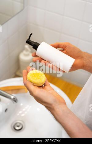 Ein Mann hat die Wahl zwischen einem festen Shampoo-Riegel und einem flüssigen. Badezimmerzubehör. Plastikfrei, kein Abfall, geringe Wassermenge. Stockfoto