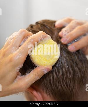 Ein Mann benutzt eine solide Shampoo-Bar im Bad. Shampoo auf die Kopfhaut auftragen. Plastikfrei, kein Abfall, geringe Wassermenge. Nachhaltig Stockfoto