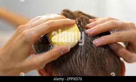 Mann im Badezimmer. Ein Mann trägt einen soliden Shampoo-Stab auf das Haar auf. Nachhaltige Haarpflege, umweltfreundliche Kosmetik. Ohne Plastik, ohne Verschwendung Stockfoto
