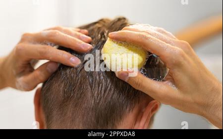 Ein Mann trägt einen soliden Shampoo-Stab auf das Haar auf. Mann im Badezimmer. Plastikfrei, kein Abfall, geringe Wassermenge. Nachhaltige Haarpflege, Eco Stockfoto