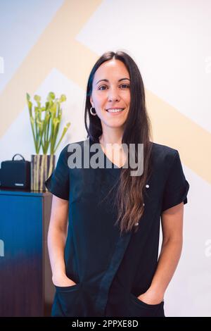 Positive Frau trägt schwarze medizinische Uniform und schaut in der Praxis auf die Kamera Stockfoto