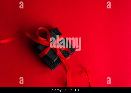 Schwarze Geschenkbox mit rotem Band auf hellrotem Hintergrund Stockfoto