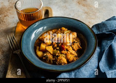 Hähnchenfleisch-Eintopf mit Gemüse in der Keramikschüssel und ein Glas Bernsteinwein Stockfoto