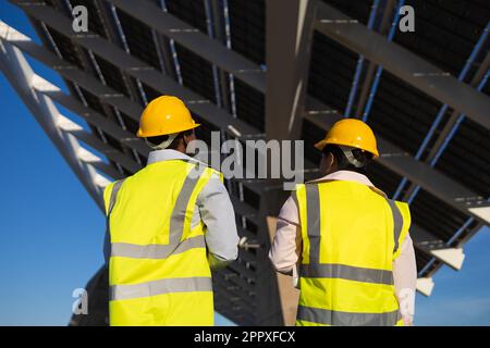 Rückansicht anonymer Ingenieure in Schutzhelmen und Uniform, die neben installierten Solarpaneelen auf der Baustelle stehen Stockfoto