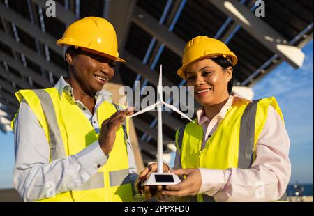 Afroamerikanische Bauerinnen in Schutzhelm und Uniform, die bei der Zusammenarbeit auf der Baustelle Windturbinen nutzen Stockfoto
