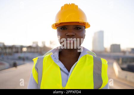 Seriöse afroamerikanische Ingenieurin in gelbem Schutzhelm und Uniform, die auf der Baustelle in die Kamera blickt Stockfoto