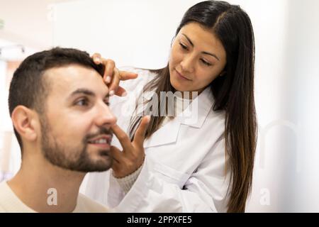 Junger Augenarzt mit langer Haarlinse im menschlichen Auge bei einem Besuch zur Augenbehandlung in der Klinik Stockfoto