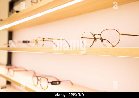 Moderne Brille mit Metallrahmen auf Holzregalen mit heller Beleuchtung in einem modernen Lichthaus Stockfoto