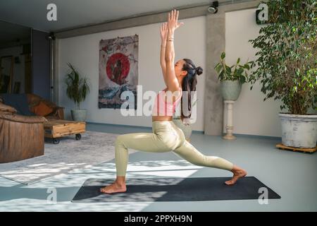 Voller Körper aus fokussierter asiatischer Passform, weiblich in Aktivbekleidung, die Ashta Chandrasana mit erhobenen Armen auf der Matte macht und Achtsamkeit während des Yoga-Kurses übt Stockfoto