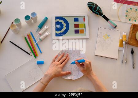 Draufsicht des anonymen Künstlers mit bunten Farben auf kreisförmigem weißem Papierbogen mit bunten Bleistiften und mit Pinsel auf Glättung malen Stockfoto
