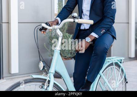 Unbekannte afroamerikanische Unternehmer, die Fahrrad gegen ein modernes Gebäude fuhren Stockfoto