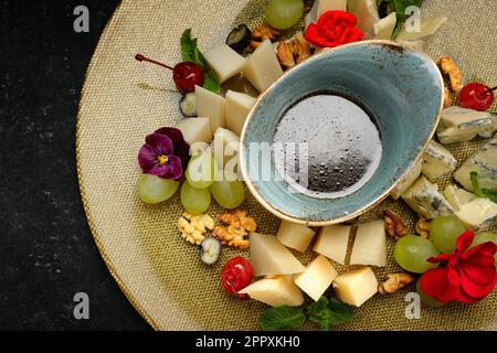 Köstliche Käseplatte mit verschiedenen Käsesorten, Trauben, Nüssen und Honig Stockfoto