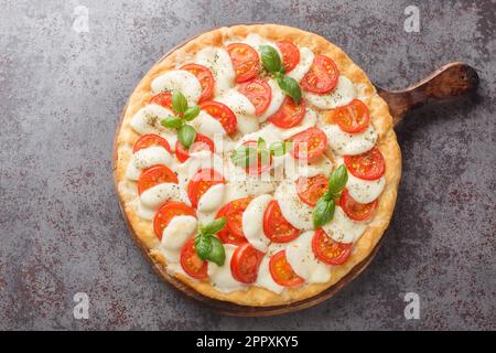 Caprese Pizza mit geschmolzenem Mozzarella, Tomaten und Basilikumblättern aus nächster Nähe auf einem Holzbrett auf dem Tisch. Horizontale Draufsicht von oben Stockfoto
