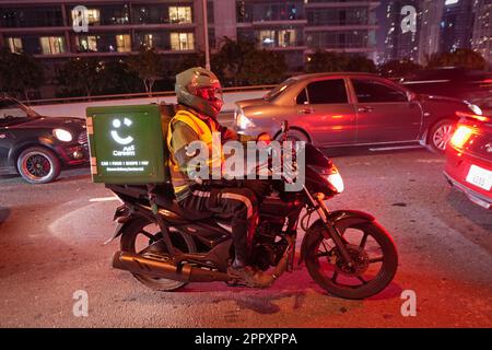 Motorradarbeiter, die Lebensmittel liefern, arbeiten auf der Straße. Dubai, Vereinigte Arabische Emirate - April 2023 Stockfoto