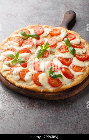 Klassische Caprese-Pizza mit Mozzarella, Tomaten und Basilikumblättern aus der Nähe auf einem Holzbrett auf dem Tisch. Vertikal Stockfoto
