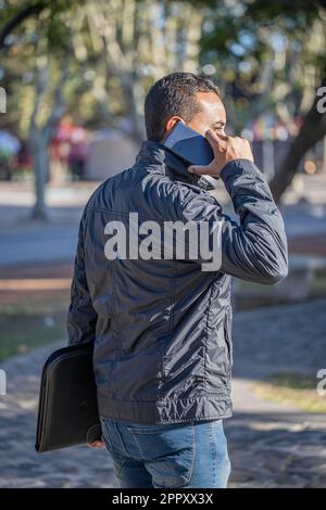 Junger Latino-Mann, der mit dem Handy spricht, von hinten gesehen. Stockfoto