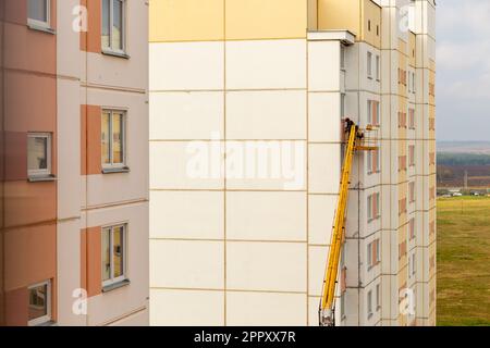 Arbeiter im Korb einer Hebebühne reparieren die Fassade des Wohngebäudes. Arbeiter in der hydraulischen Hebebühne reparieren den Balkon. Baumeister auf li Stockfoto