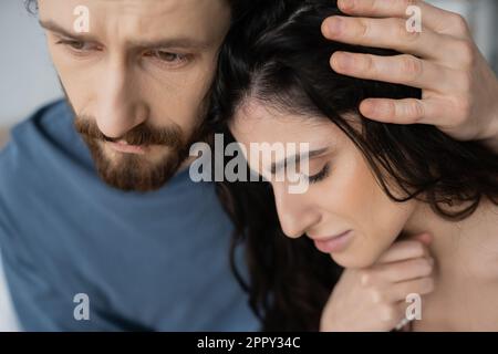 Bärtiger Mann, der sich beruhigt und verärgerte Freundin zu Hause umarmt, Image der Börse Stockfoto