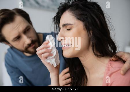 Verschwommener Mann, der sich beruhigt, verärgert und weinende Freundin mit Serviette zu Hause, Börsenbild Stockfoto