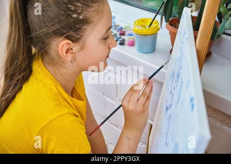 Das niedliche kleine Mädchen, das auf die Staffelei malt. Stockfoto