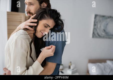 Empathischer Mann beruhigt weinende Freundin in verschwommenem Schlafzimmer zu Hause, Stock Image Stockfoto