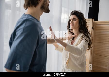 Eine verängstigte Frau, die zu Hause eine Stoppgeste in der Nähe eines missbräuchlichen Freundes zeigt, ein Aktienbild Stockfoto