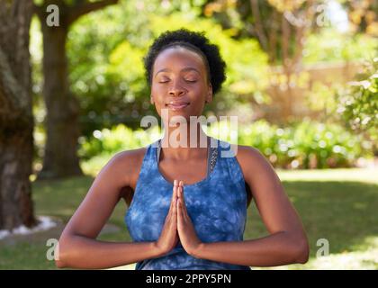 Junge Schwarze sitzt draußen in Yoga-Pose, Hände im Gebet meditieren Stockfoto