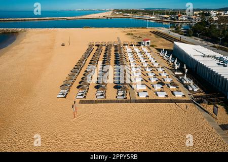 Draufsicht auf Strohschirme und Sonnenliegen am Strand von Vilamoura, Algarve, Portugal Stockfoto