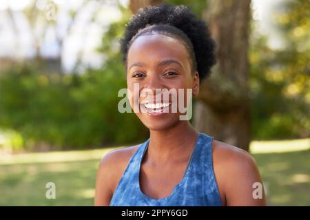Porträt einer wunderschönen schwarzen Frau, die im Park, auf Bäumen und im Rasen lächelt Stockfoto