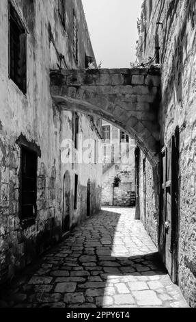 Steingebäude in einer alten gepflasterten Seitenstraße in der Altstadt von Acre, Haifa - Israel - B&W Stockfoto