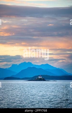 Eldred Rock Lighthouse bei Sonnenuntergang mit dramatischer Bergkette im Hintergrund, neben dem Lynn Canal in Alaska Stockfoto