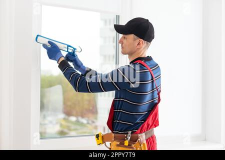Bauarbeiter versiegelt Fenster mit Versiegelung in Innenräumen Stockfoto
