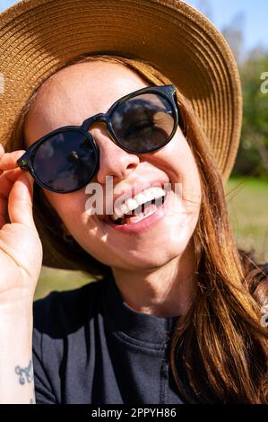 Nahaufnahme einer glücklichen jungen Frau mit Sonnenbrille und Strohhut. Stockfoto