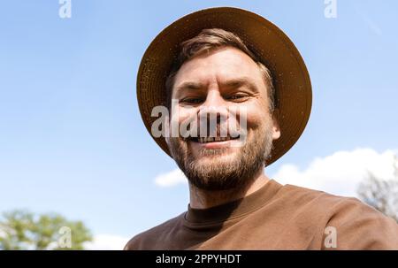 Ein bärtiger Mann mit Strohhut, der in die Kamera schaut und lächelt. Stockfoto