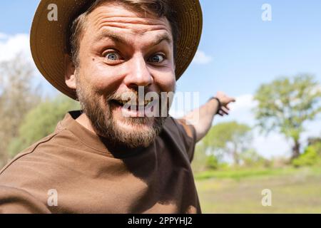 Reise-Video-Blogger Vlogging in wilder Natur, Mann trägt Strohhut mit erfreulichem Gesichtsausdruck auf Reisen in der Natur Stockfoto