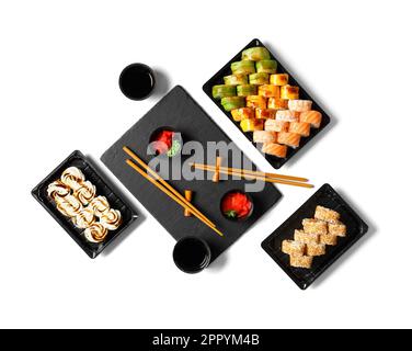 Sushi-Brötchen in Plastikpackungen mit Sojasoße, Ingwer und Wasabi auf weißem Hintergrund, Draufsicht. Sushi-Abgabe im Kunststoffbehälter Stockfoto