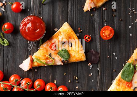 Pizzastücke mit Jerky, Oliven, Käse und Kräutern werden auf dunklem Holzhintergrund, einem Zweig frischer Kirschtomaten und Saucen aufgetragen Stockfoto
