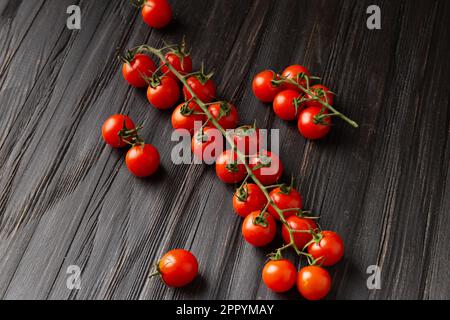 Kirschtomaten auf einem Zweig auf einem dunklen Holzhintergrund von oben. Frische Kirschtomaten auf Holzhintergrund. Gesundes Essen. Veganismus. Stockfoto